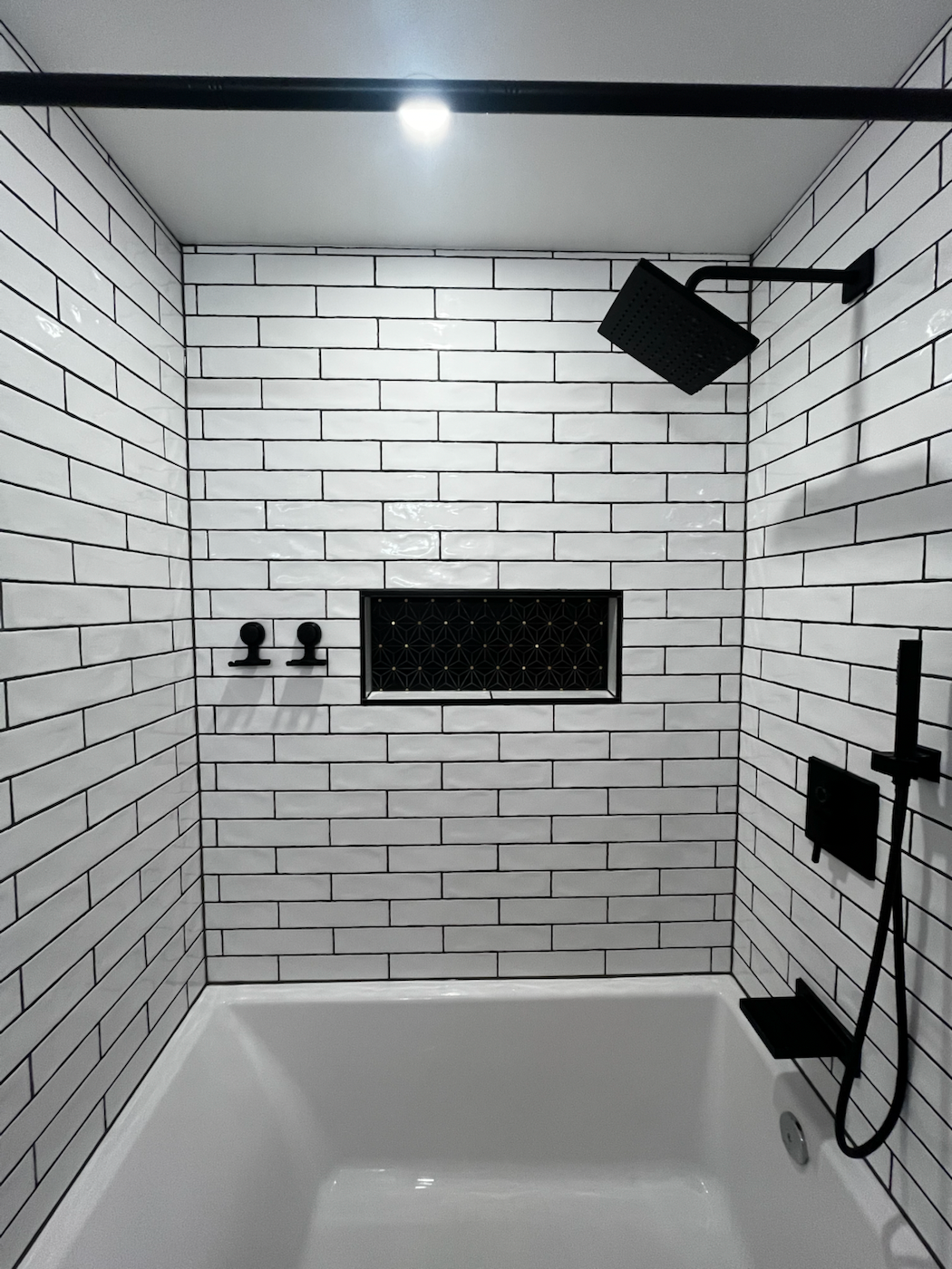 White subway tile shower with black fixtures and inset niche.