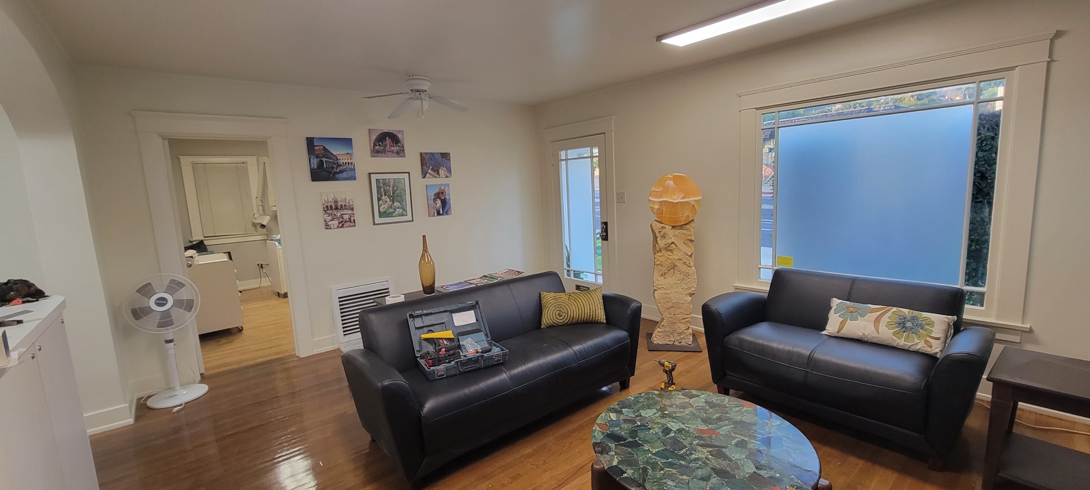 Updated living room with dark sofas, wood floors, and large windows.